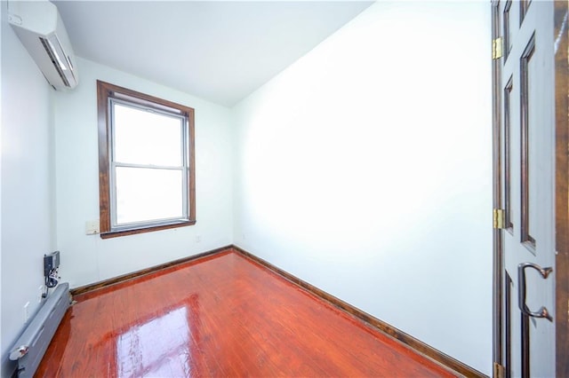 unfurnished room with a baseboard heating unit, an AC wall unit, wood finished floors, and baseboards