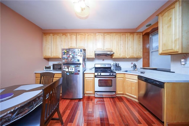 kitchen featuring light brown cabinetry, a sink, under cabinet range hood, dark wood-style floors, and appliances with stainless steel finishes