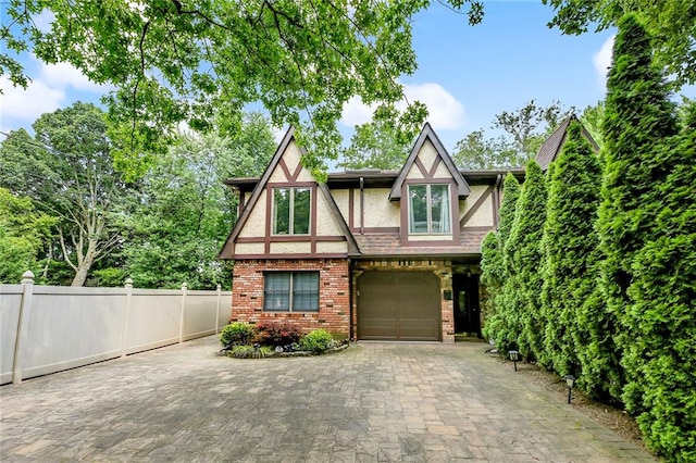 tudor home featuring brick siding, fence, stucco siding, decorative driveway, and a garage