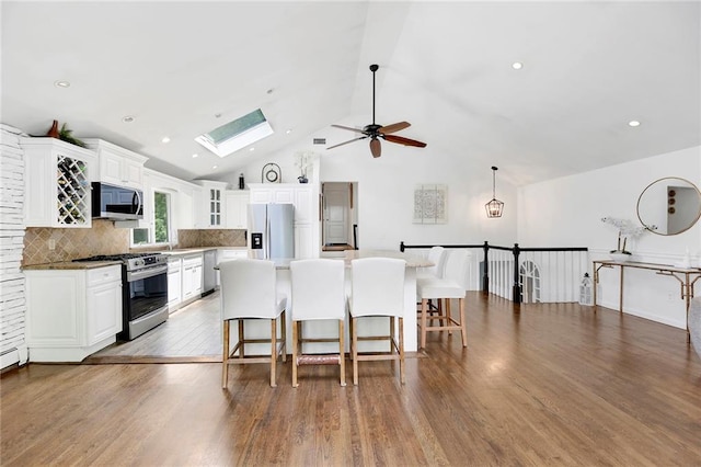 kitchen with a breakfast bar area, wood finished floors, a ceiling fan, a skylight, and stainless steel appliances