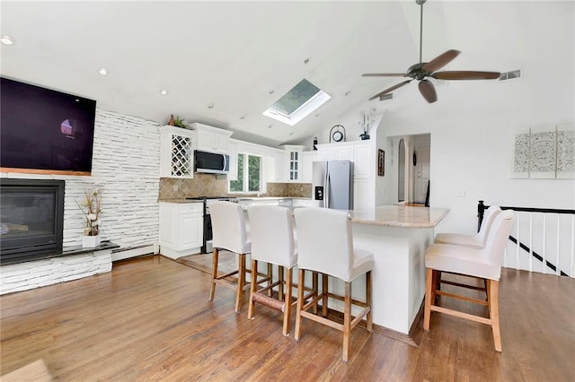 kitchen featuring visible vents, appliances with stainless steel finishes, a skylight, a kitchen breakfast bar, and wood finished floors