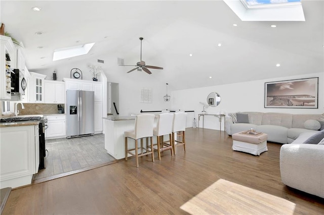 living room with visible vents, light wood-type flooring, a skylight, high vaulted ceiling, and a ceiling fan