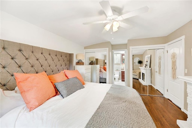 bedroom with wood finished floors, ensuite bath, ceiling fan, vaulted ceiling, and multiple closets