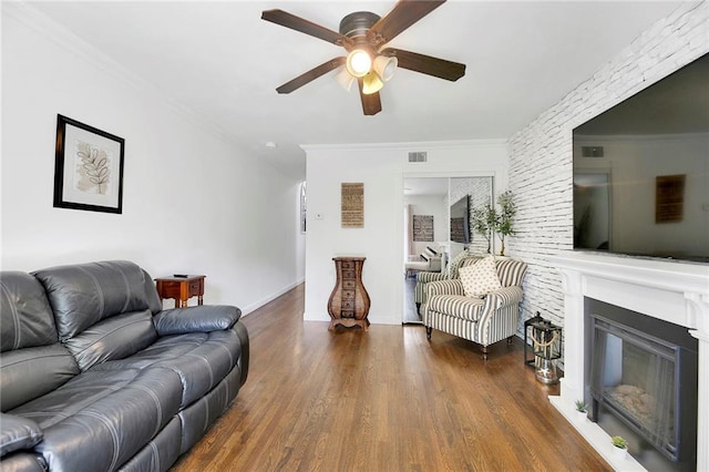 living area with visible vents, crown molding, a glass covered fireplace, wood finished floors, and a ceiling fan