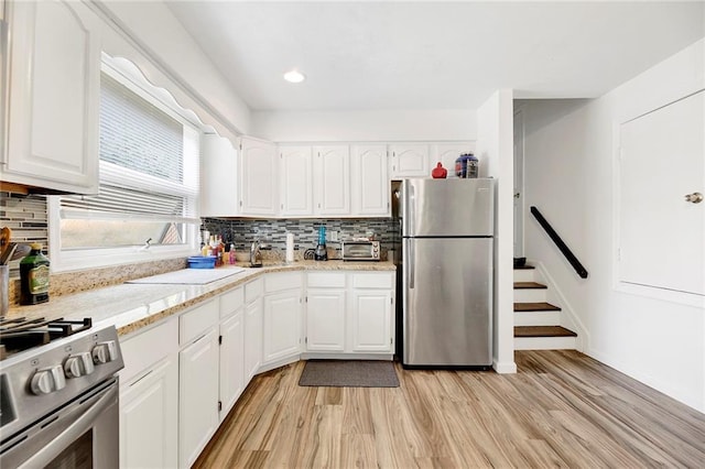 kitchen featuring backsplash, white cabinets, light wood finished floors, and appliances with stainless steel finishes