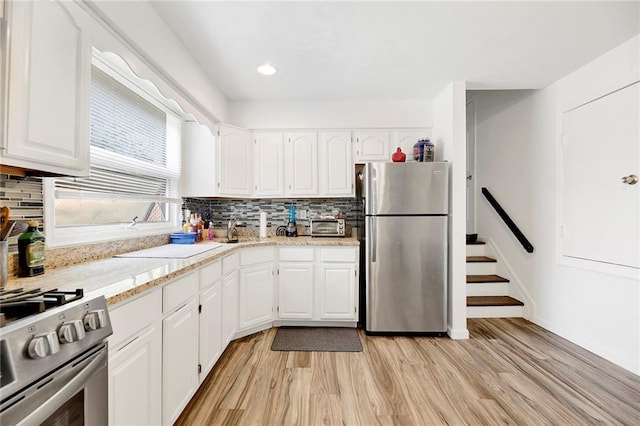 kitchen featuring light wood-type flooring, white cabinetry, appliances with stainless steel finishes, and backsplash