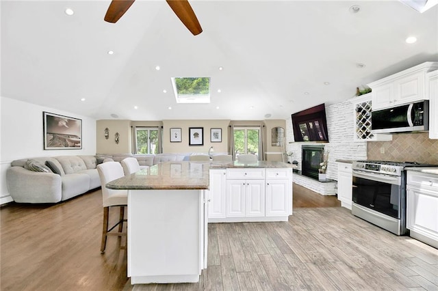 kitchen featuring light stone countertops, open floor plan, a breakfast bar area, light wood-type flooring, and appliances with stainless steel finishes