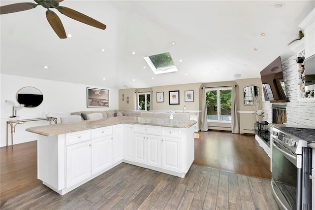 kitchen with ceiling fan, open floor plan, vaulted ceiling with skylight, stainless steel stove, and dark wood-style floors