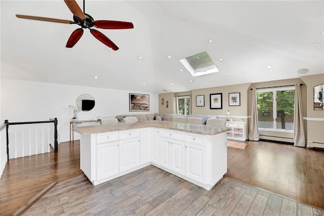 kitchen with light stone counters, light wood-style flooring, ceiling fan, white cabinets, and open floor plan