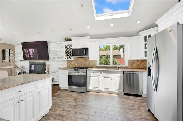 kitchen with decorative backsplash, light wood-style flooring, a skylight, stainless steel appliances, and a sink