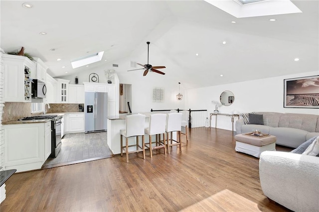 living area with ceiling fan, high vaulted ceiling, a skylight, and light wood finished floors