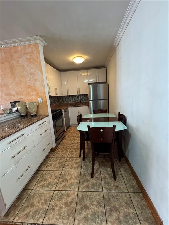 kitchen with appliances with stainless steel finishes, tasteful backsplash, white cabinets, tile patterned flooring, and baseboards