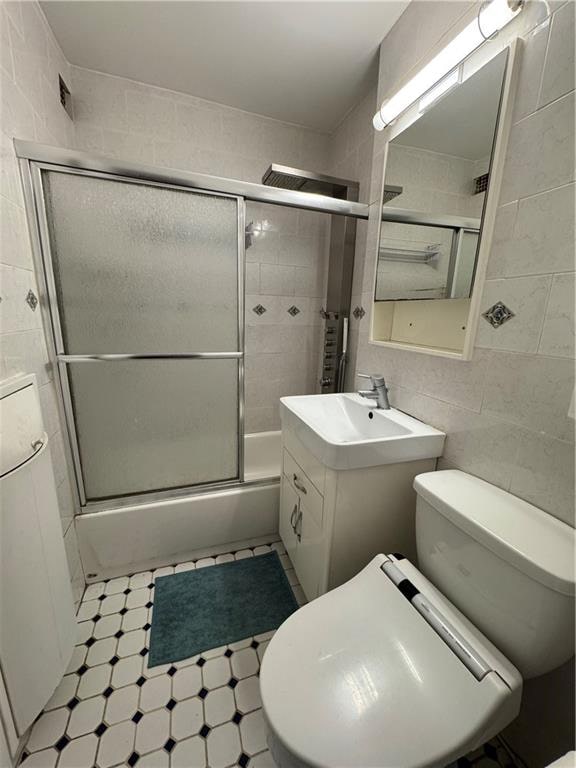 full bath with tile walls, toilet, tile patterned floors, vanity, and shower / bath combination with glass door