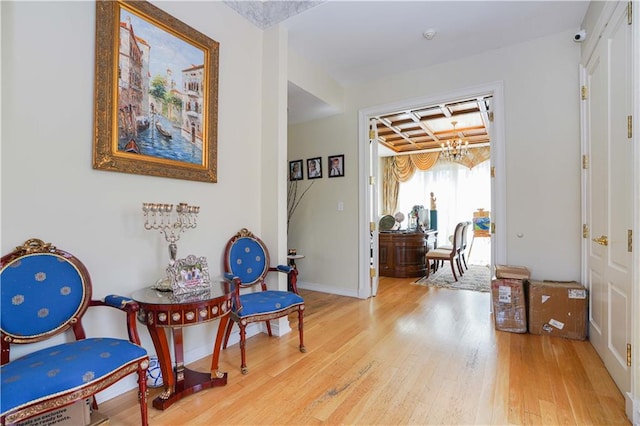 sitting room with baseboards, wood-type flooring, a notable chandelier, and coffered ceiling