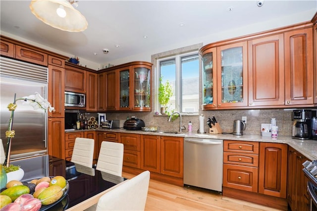 kitchen featuring tasteful backsplash, glass insert cabinets, built in appliances, light wood-type flooring, and a sink