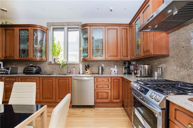 kitchen featuring wall chimney range hood, brown cabinets, and appliances with stainless steel finishes