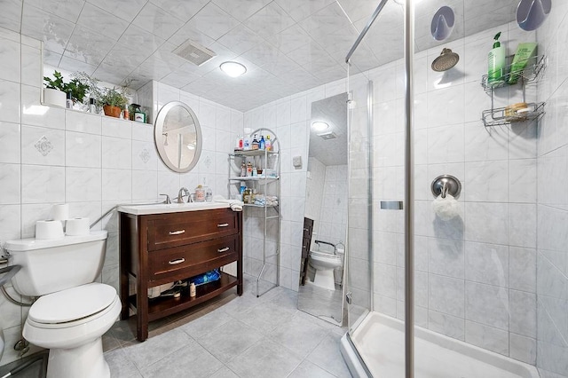 full bath with toilet, vanity, a stall shower, tile patterned floors, and tile walls