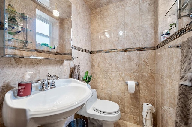 bathroom featuring a sink, toilet, and tile walls