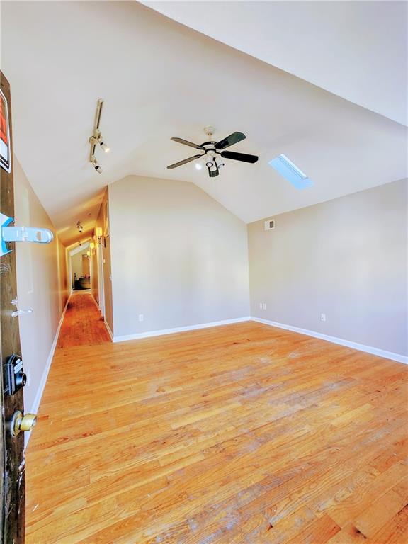 interior space featuring visible vents, a ceiling fan, light wood finished floors, baseboards, and vaulted ceiling