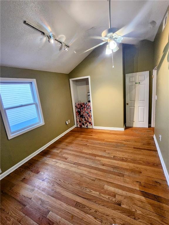 empty room with lofted ceiling, wood finished floors, baseboards, and ceiling fan