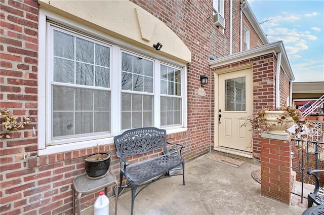 view of exterior entry featuring brick siding and a patio