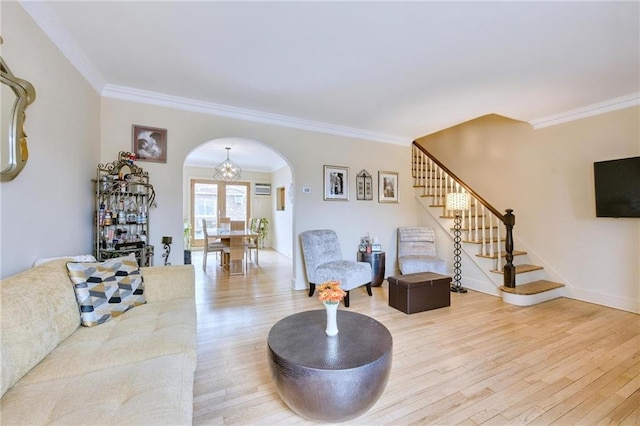 living room featuring stairs, light wood-style flooring, arched walkways, and ornamental molding