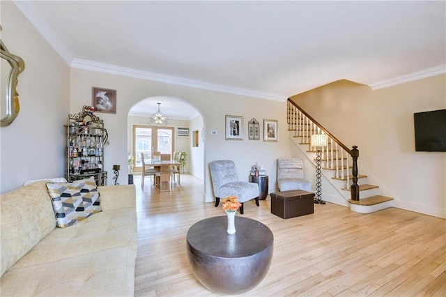 living room with arched walkways, ornamental molding, light wood finished floors, and stairs