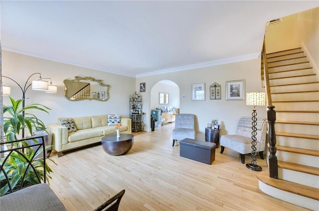 living area with arched walkways, light wood-style flooring, stairway, and ornamental molding