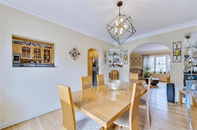 dining space featuring an inviting chandelier, crown molding, arched walkways, baseboards, and light wood-style floors