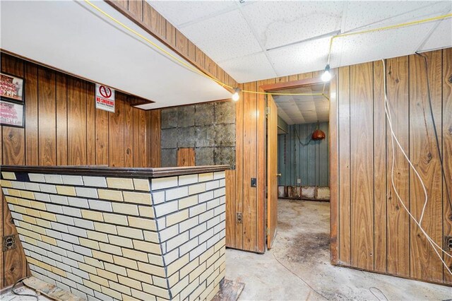 bar with wood walls, a bar, concrete flooring, and a paneled ceiling