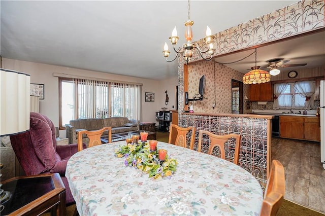 dining area with wallpapered walls, dark wood-type flooring, ceiling fan with notable chandelier, and a healthy amount of sunlight