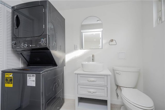 half bath featuring baseboards, vanity, toilet, and stacked washer / dryer