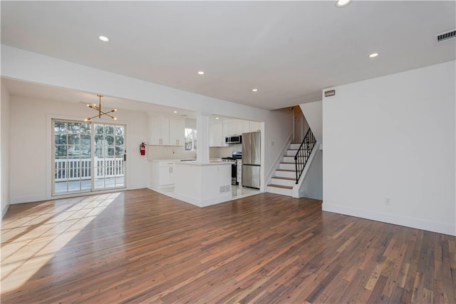 unfurnished living room with a notable chandelier, recessed lighting, stairs, and wood-type flooring