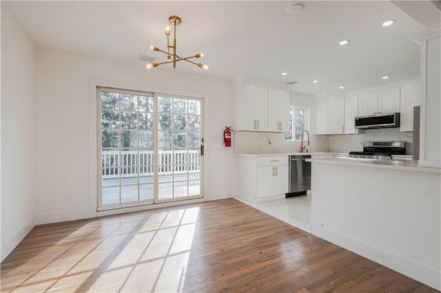 kitchen with an inviting chandelier, tasteful backsplash, white cabinetry, light countertops, and stainless steel appliances
