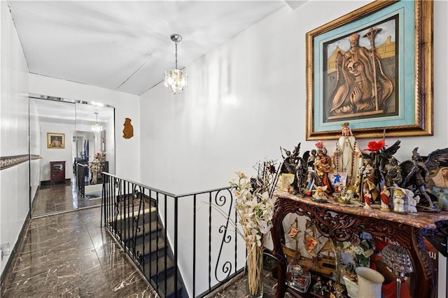 hall with an upstairs landing, marble finish floor, and an inviting chandelier