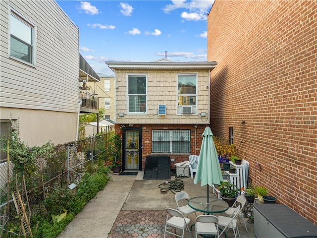 rear view of property featuring a patio area, outdoor dining space, brick siding, and fence