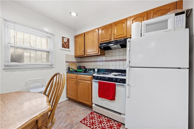 kitchen featuring white appliances, light tile patterned floors, brown cabinetry, under cabinet range hood, and backsplash