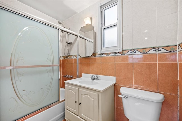 full bathroom featuring shower / bath combination with glass door, tile walls, vanity, and toilet