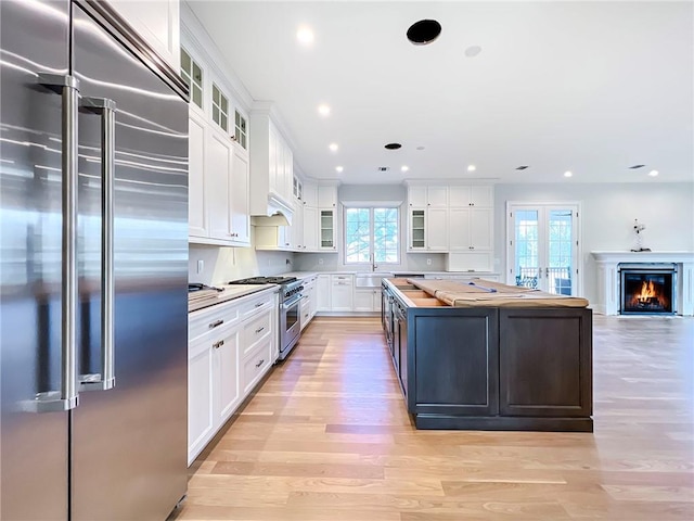 kitchen with butcher block counters, light wood-style flooring, a sink, premium appliances, and a center island