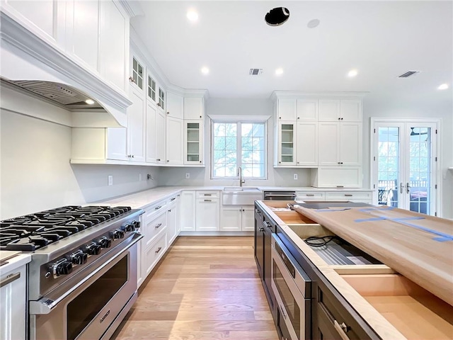 kitchen featuring premium range hood, visible vents, high end stove, a sink, and french doors