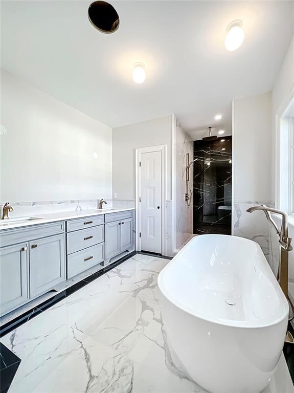 full bath with marble finish floor, a freestanding tub, tiled shower, and a sink