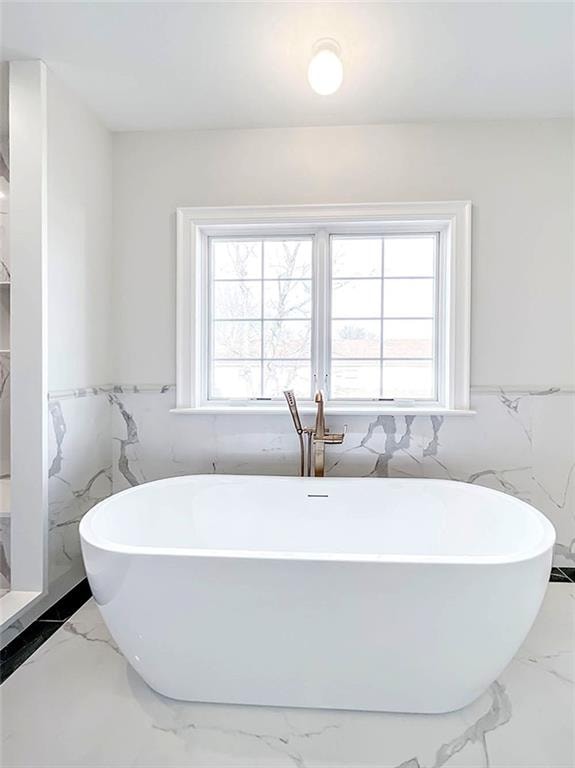 full bathroom featuring a wealth of natural light, a freestanding tub, marble finish floor, and a wainscoted wall