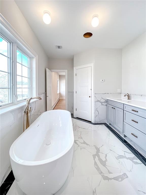 bathroom featuring visible vents, a freestanding bath, marble finish floor, and a wainscoted wall