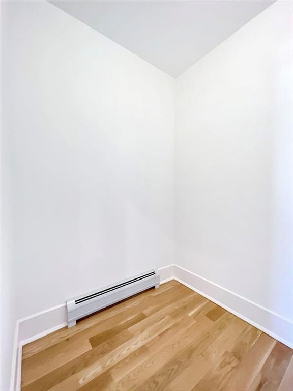 unfurnished room featuring a baseboard heating unit, light wood-style floors, and baseboards