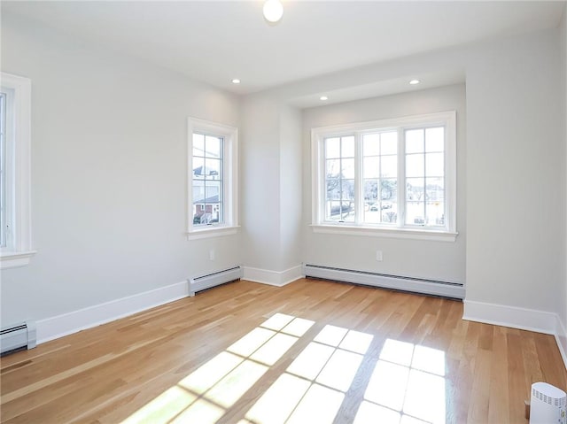 spare room featuring a baseboard heating unit, a healthy amount of sunlight, and light wood finished floors