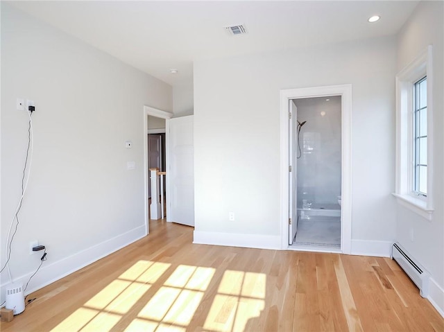 empty room featuring visible vents, light wood-type flooring, a baseboard heating unit, and baseboards