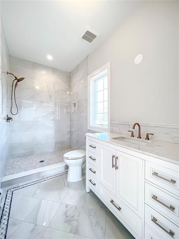 full bath featuring visible vents, toilet, tile walls, tiled shower, and vanity