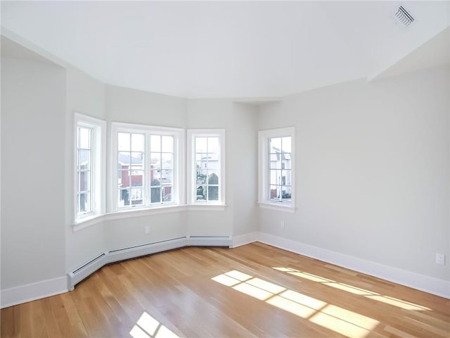 empty room featuring light wood-style floors, baseboards, baseboard heating, and visible vents