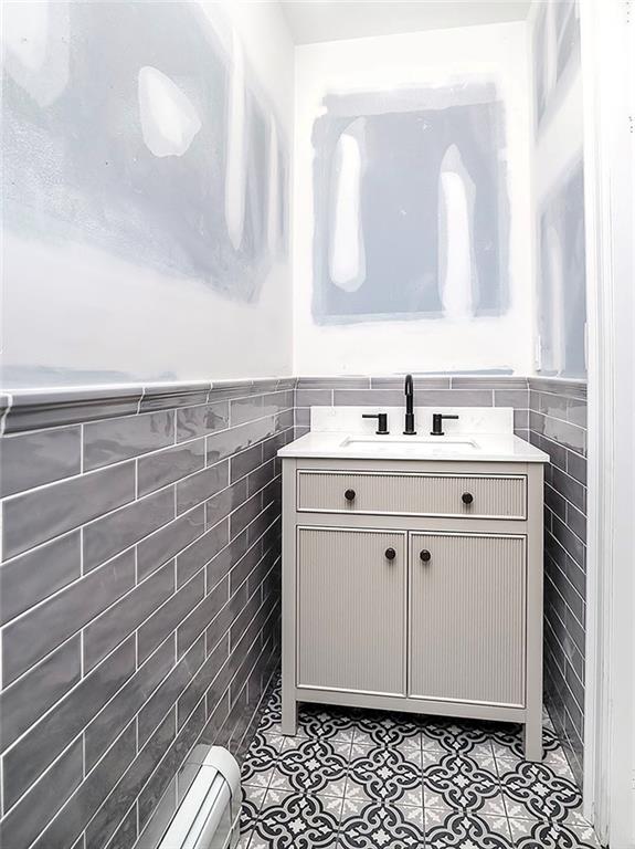 bathroom featuring vanity, wainscoting, tile patterned floors, tile walls, and a baseboard radiator