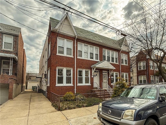 townhome / multi-family property with brick siding, an outbuilding, roof with shingles, and fence